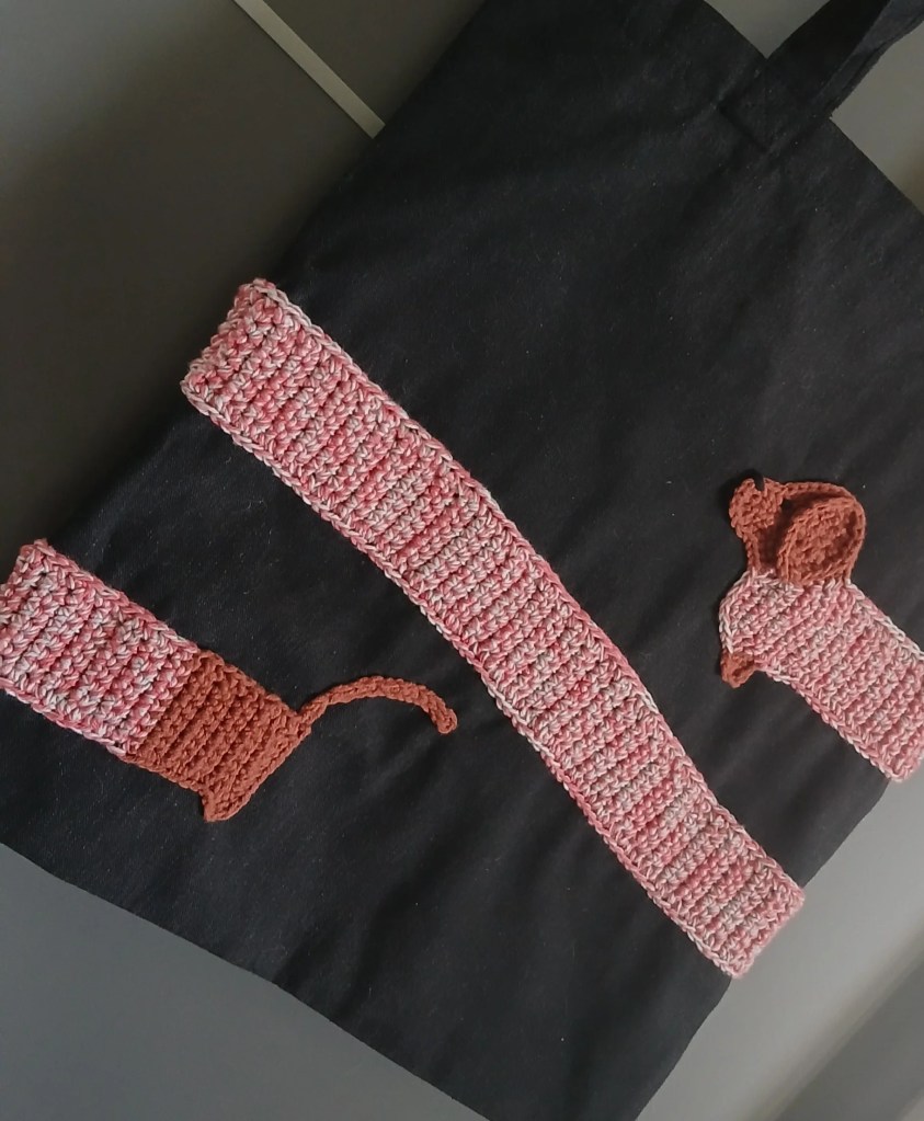 A black tote bag with crocheted dachshund wrapped around it.